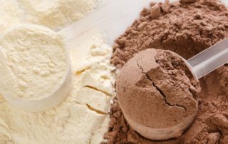 Close-up of grass-fed whey protein powders: Vanilla and Chocolate flavors on a table with visible scoops.